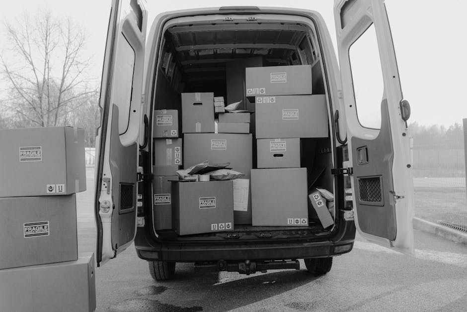 The image shows the open rear doors of a white van used for home relocation, revealing a neatly packed interior filled with various cardboard boxes of different sizes, some labeled with 'FRAGILE' stic